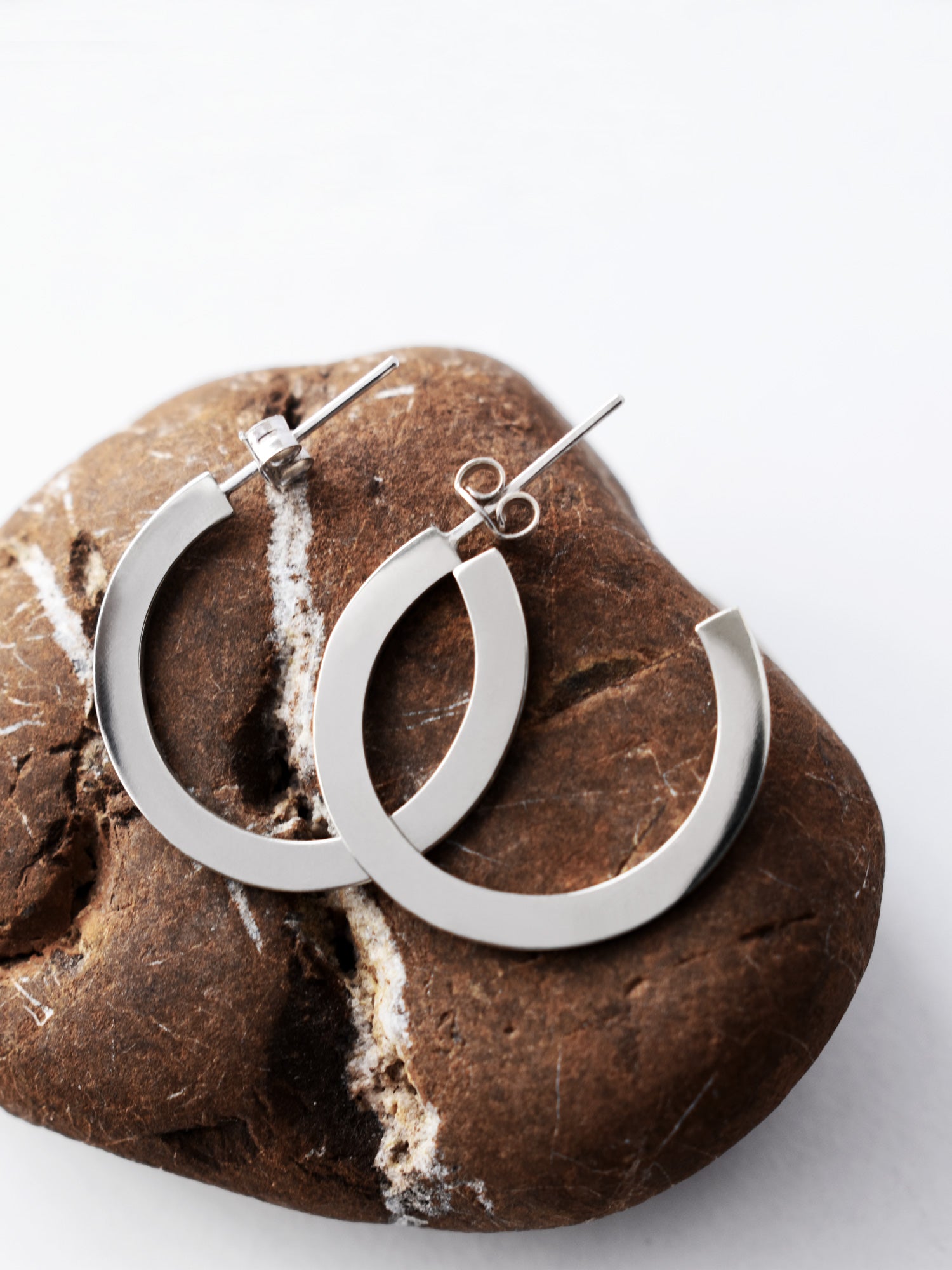 Pair of silver hoop earrings on a textured brown stone