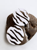 Pair of round silver stud earrings with flowing cutouts on a textured brown stone