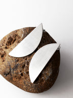 Pair of brushed silver semicircle stud earrings on a textured brown stone