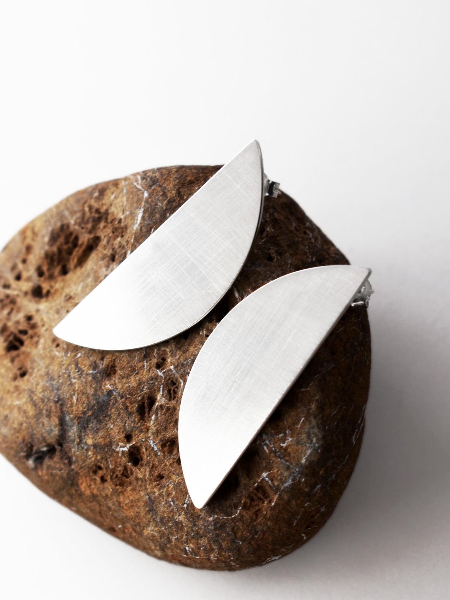 Pair of brushed silver semicircle stud earrings on a textured brown stone