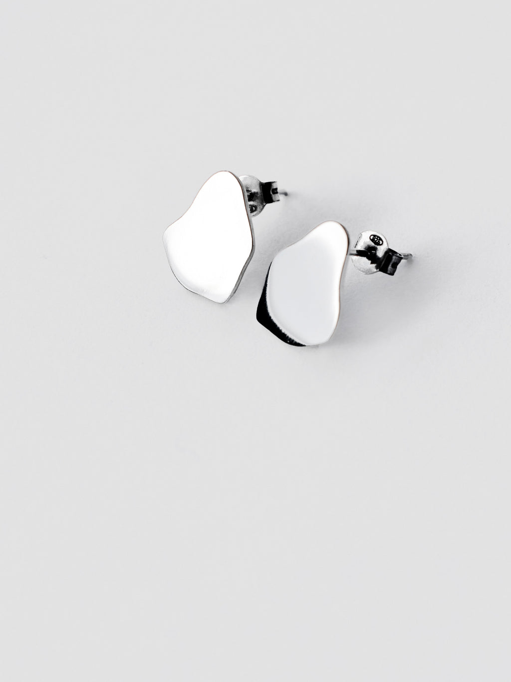 Pair of small organic-shaped silver stud earrings on a light gray background