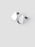 Pair of small organic-shaped silver stud earrings on a light gray background
