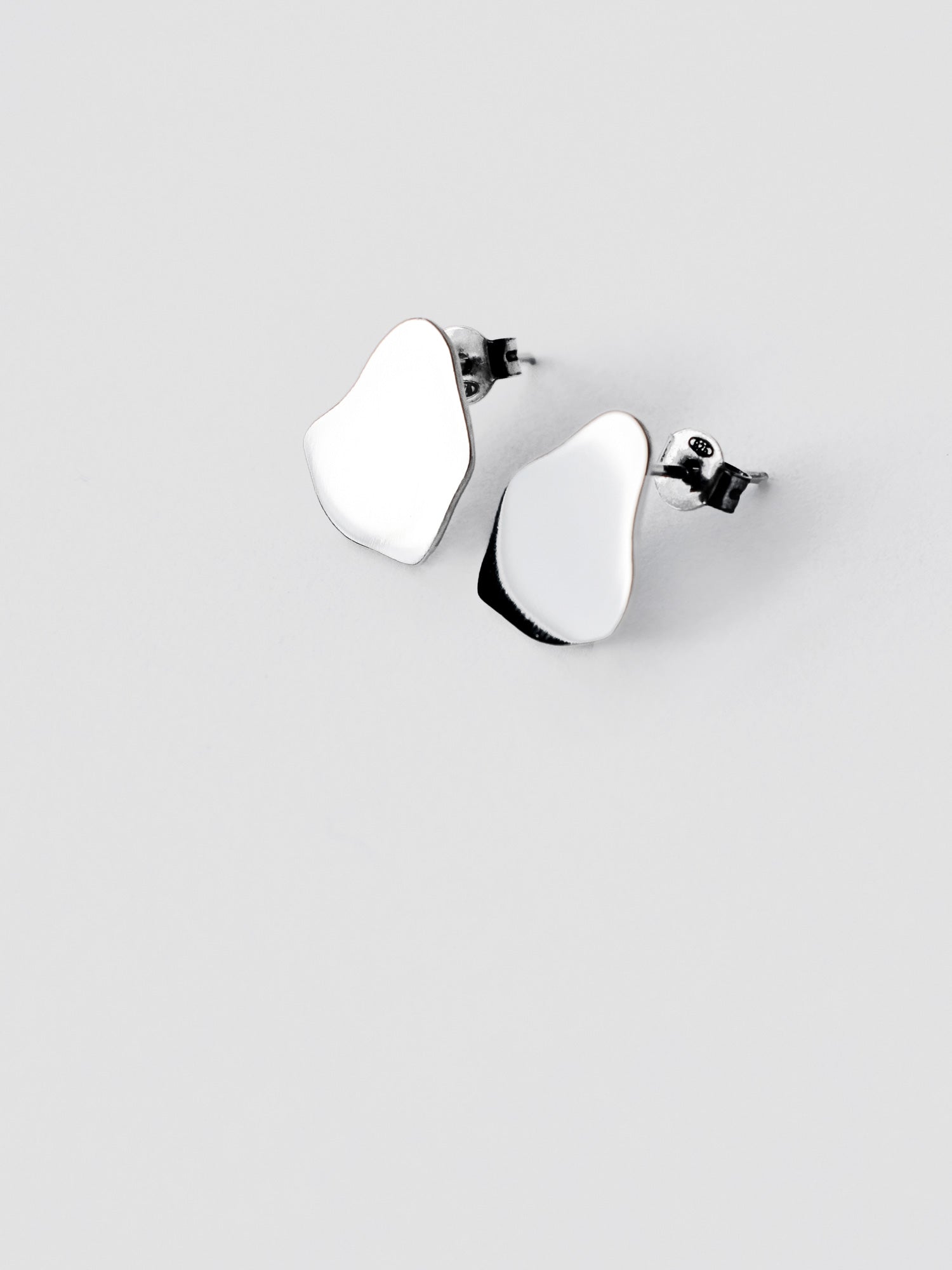 Pair of small organic-shaped silver stud earrings on a light gray background