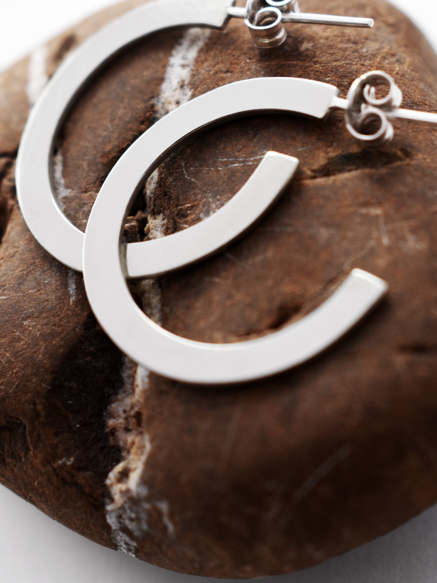 Close-up of Pair of silver hoop earrings on a textured brown stone