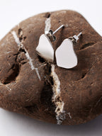Pair of small organic-shaped silver stud earrings on a textured brown stone