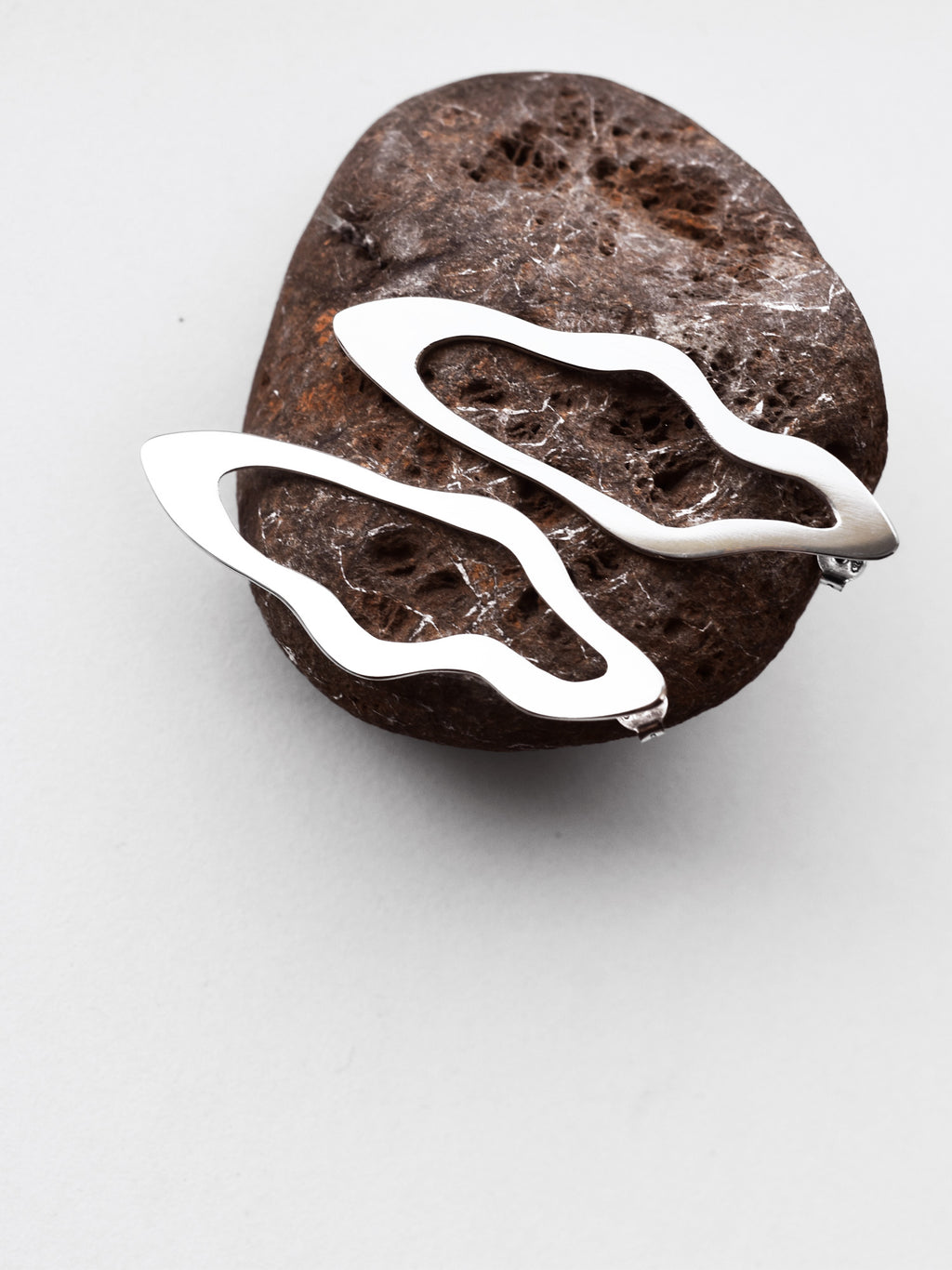 Pair of unique, organic-shaped silver stud earrings on a textured brown stone
