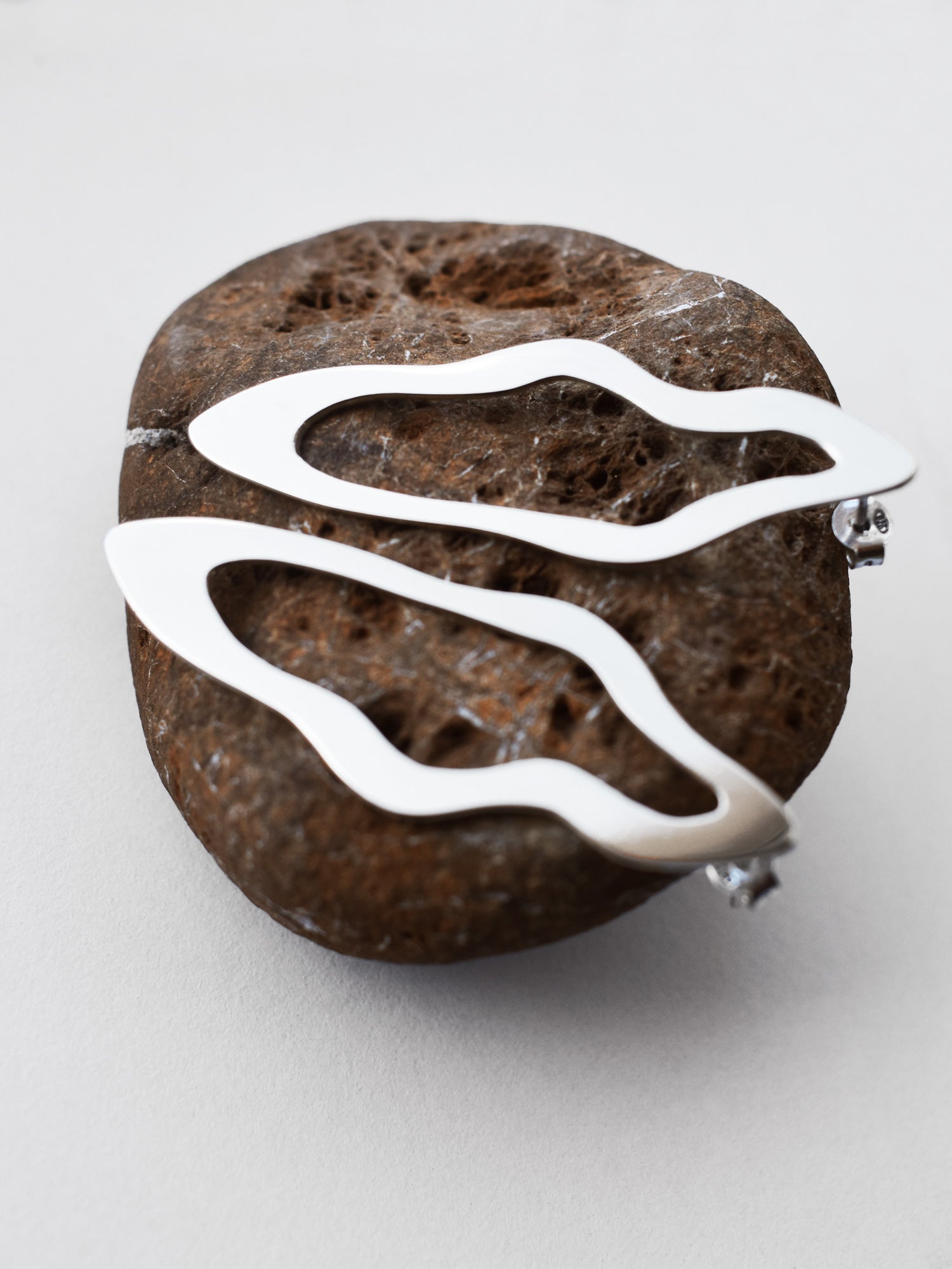Pair of unique, organic-shaped silver stud earrings on a textured brown stone