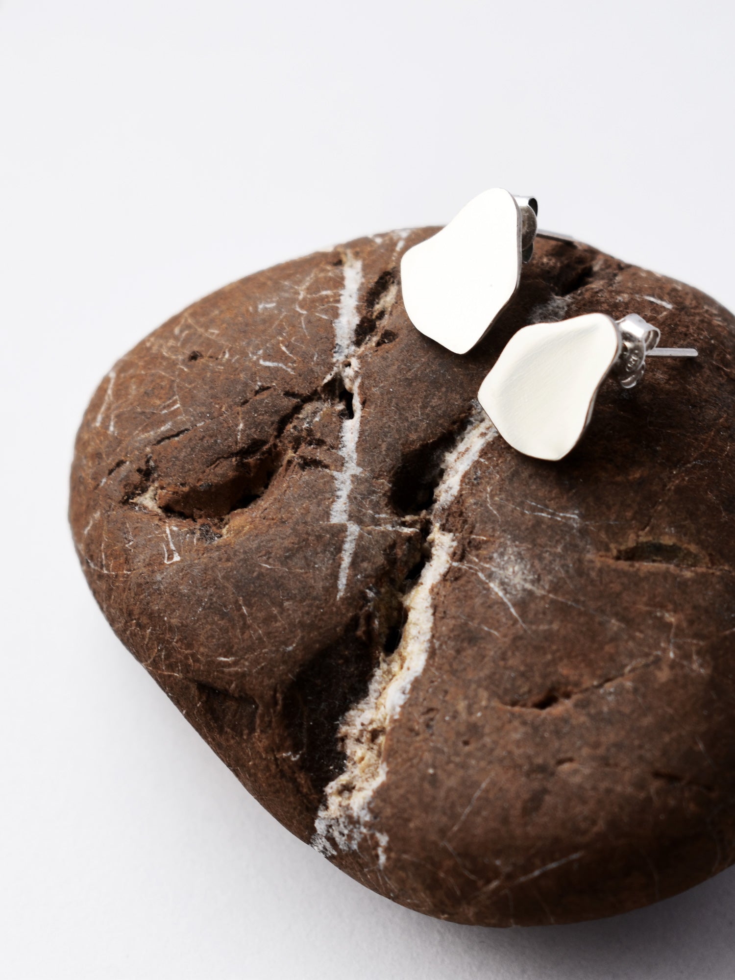 Pair of small organic-shaped silver stud earrings on a textured brown stone