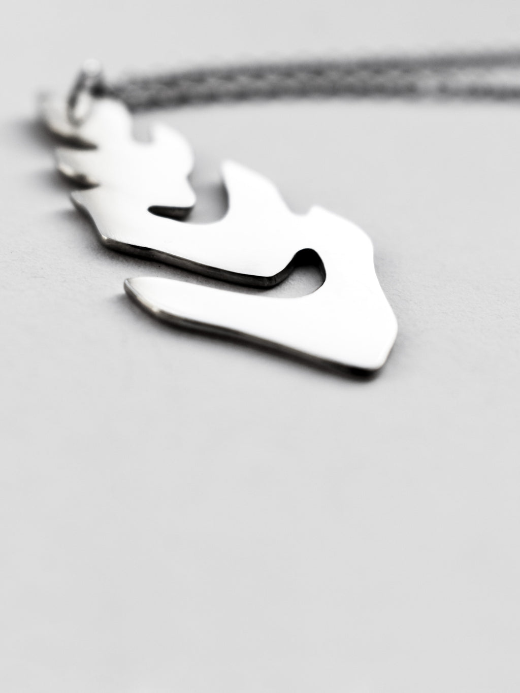 Close-up of a silver leaf-shaped pendant with chain on a light gray background