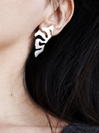 Close-up of a woman wearing an organic-shaped silver stud earring with cutout details 