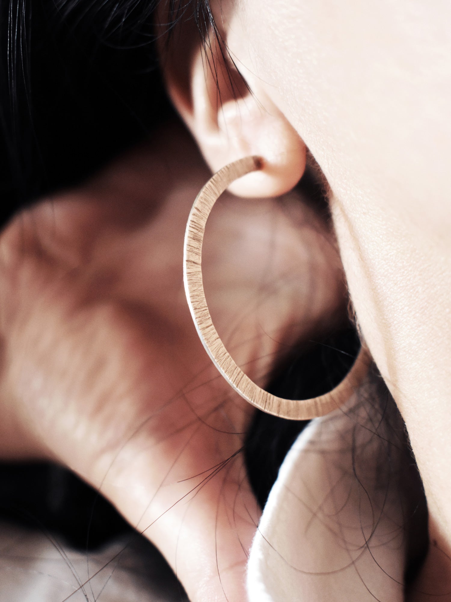 Close-up of a textured silver hoop earring worn by a woman