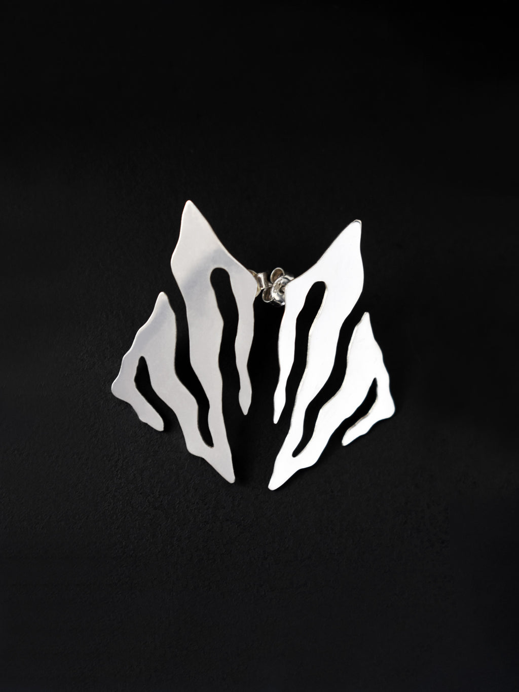 Pair of abstract-shaped silver stud earrings with flowing cutouts on a black background
