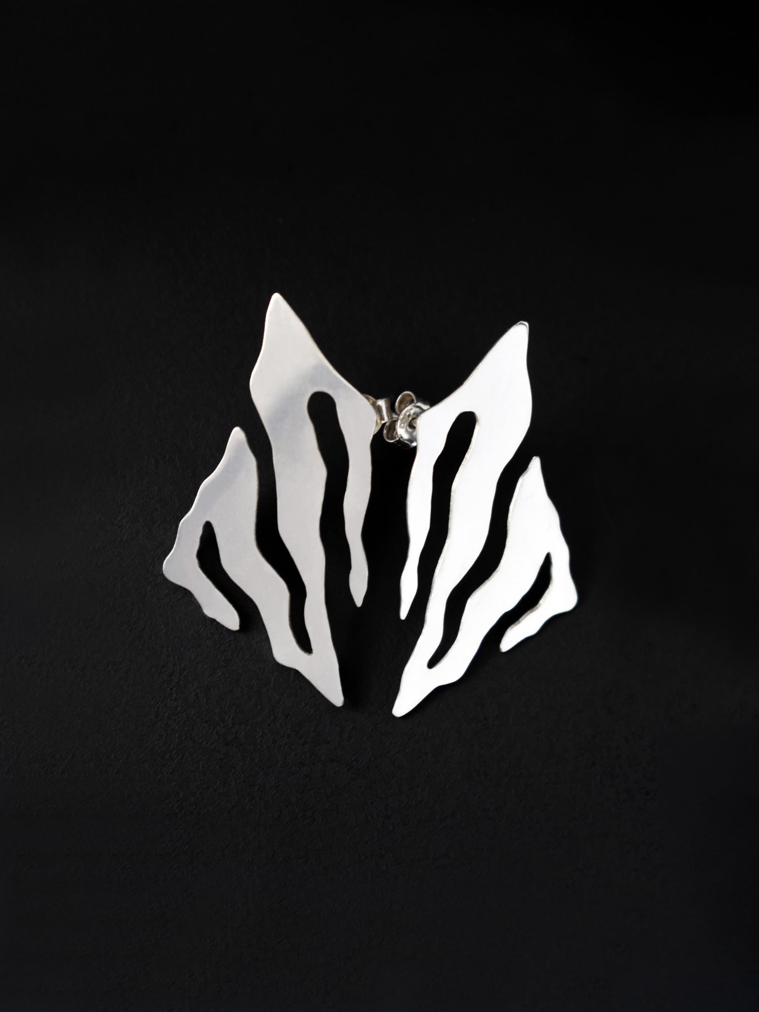 Pair of abstract-shaped silver stud earrings with flowing cutouts on a black background