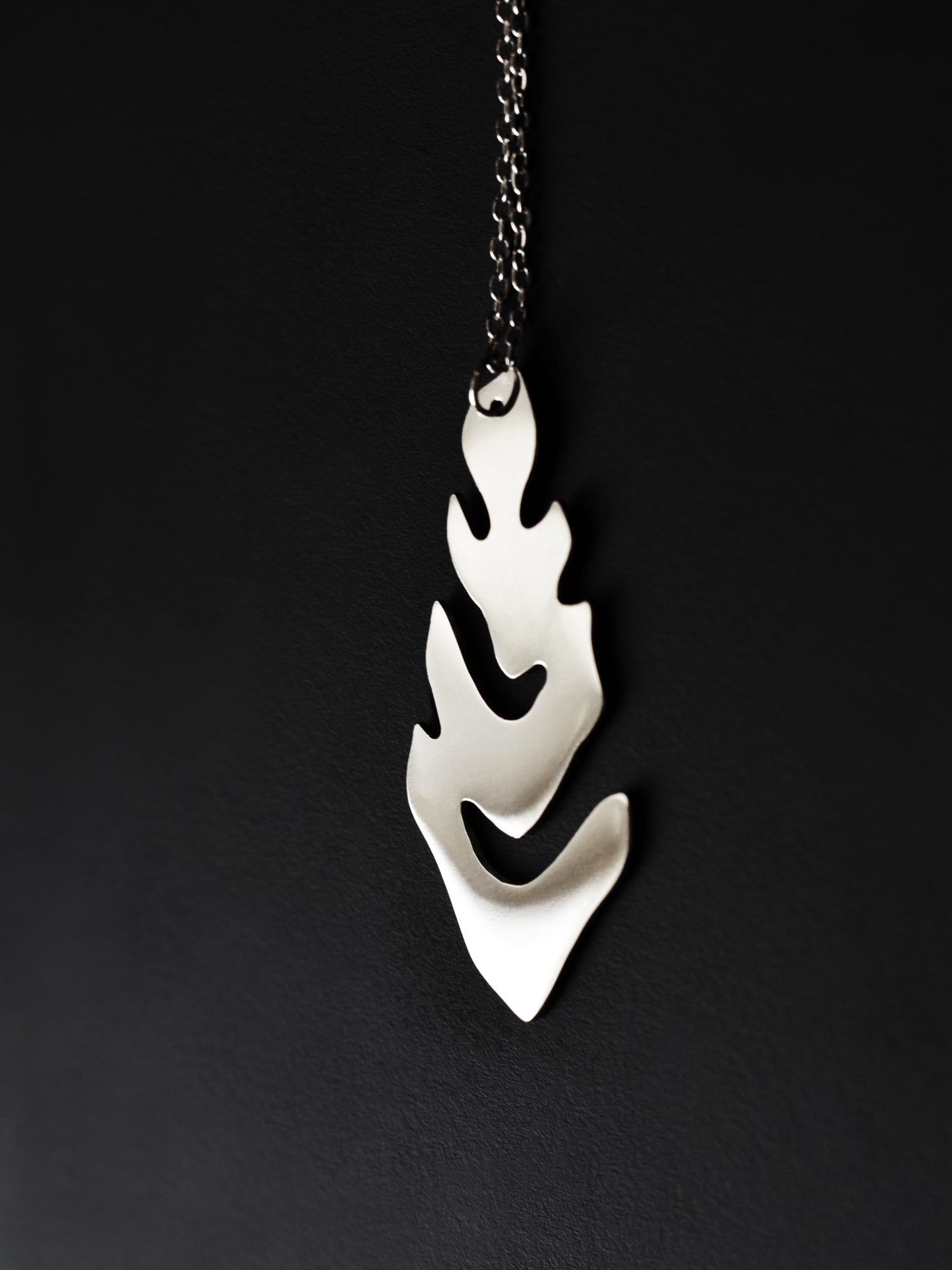 Silver leaf-shaped pendant with chain on a black background
