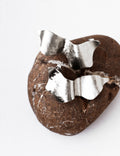 Pair of sculptural silver stud earrings on a textured brown stone