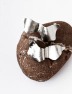 Pair of sculptural silver stud earrings on a textured brown stone