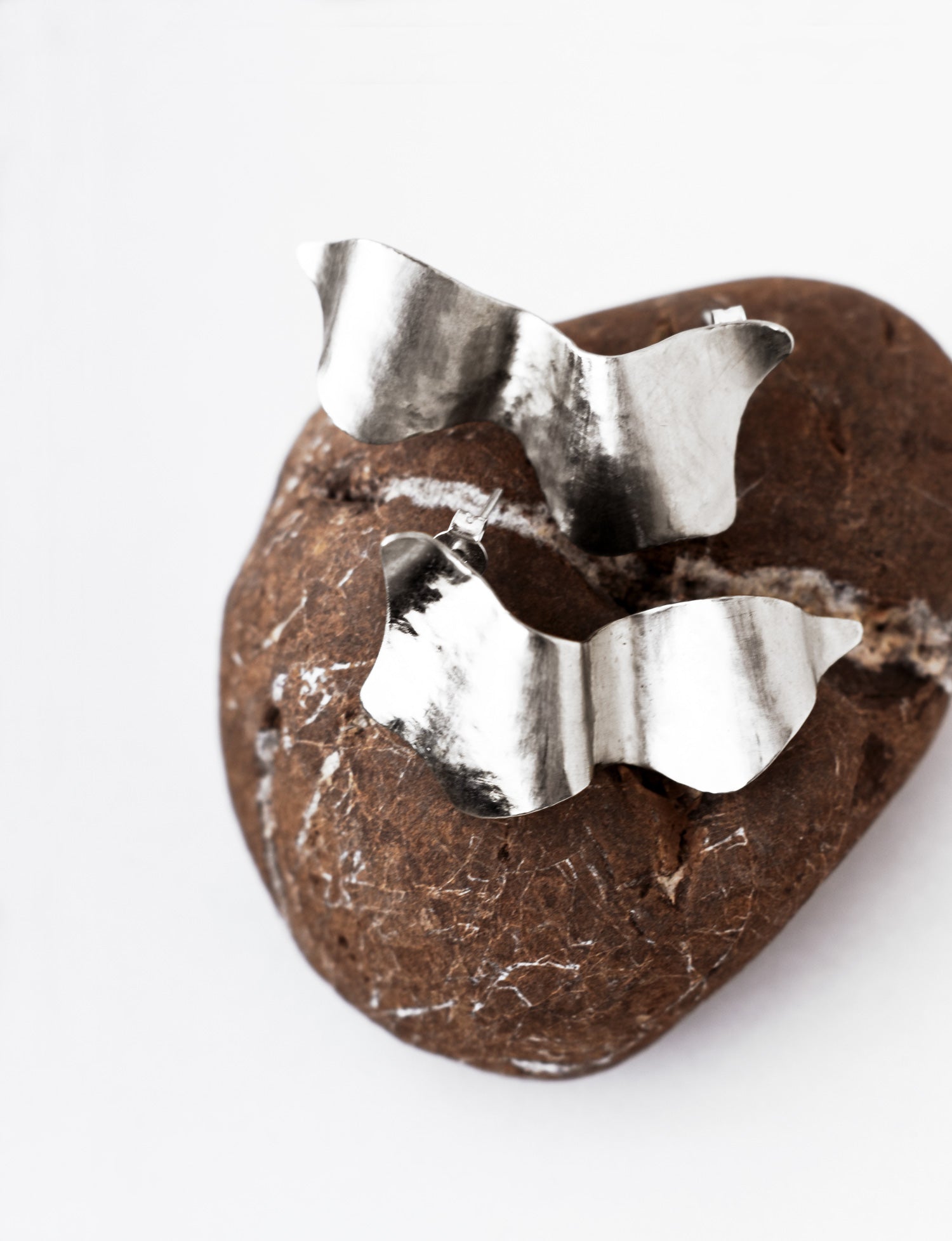 Pair of sculptural silver stud earrings on a textured brown stone