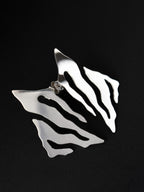 Pair of abstract-shaped silver stud earrings with flowing cutouts on a black background