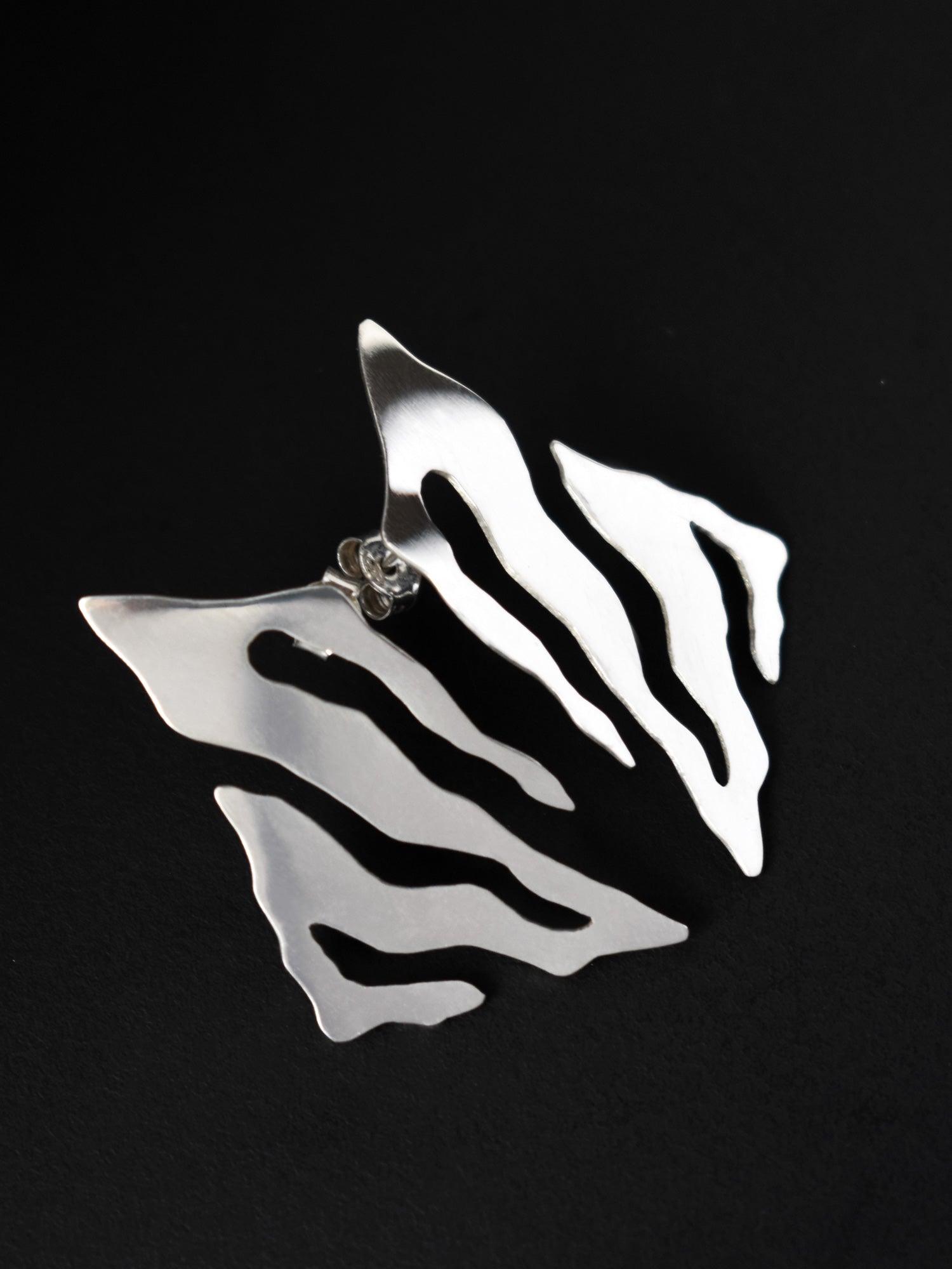 Pair of abstract-shaped silver stud earrings with flowing cutouts on a black background