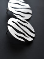 Close-up of pair of round silver stud earrings with flowing cutouts on a black background