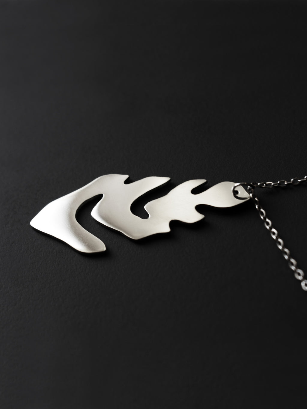 Silver leaf-shaped pendant with chain on a black background
