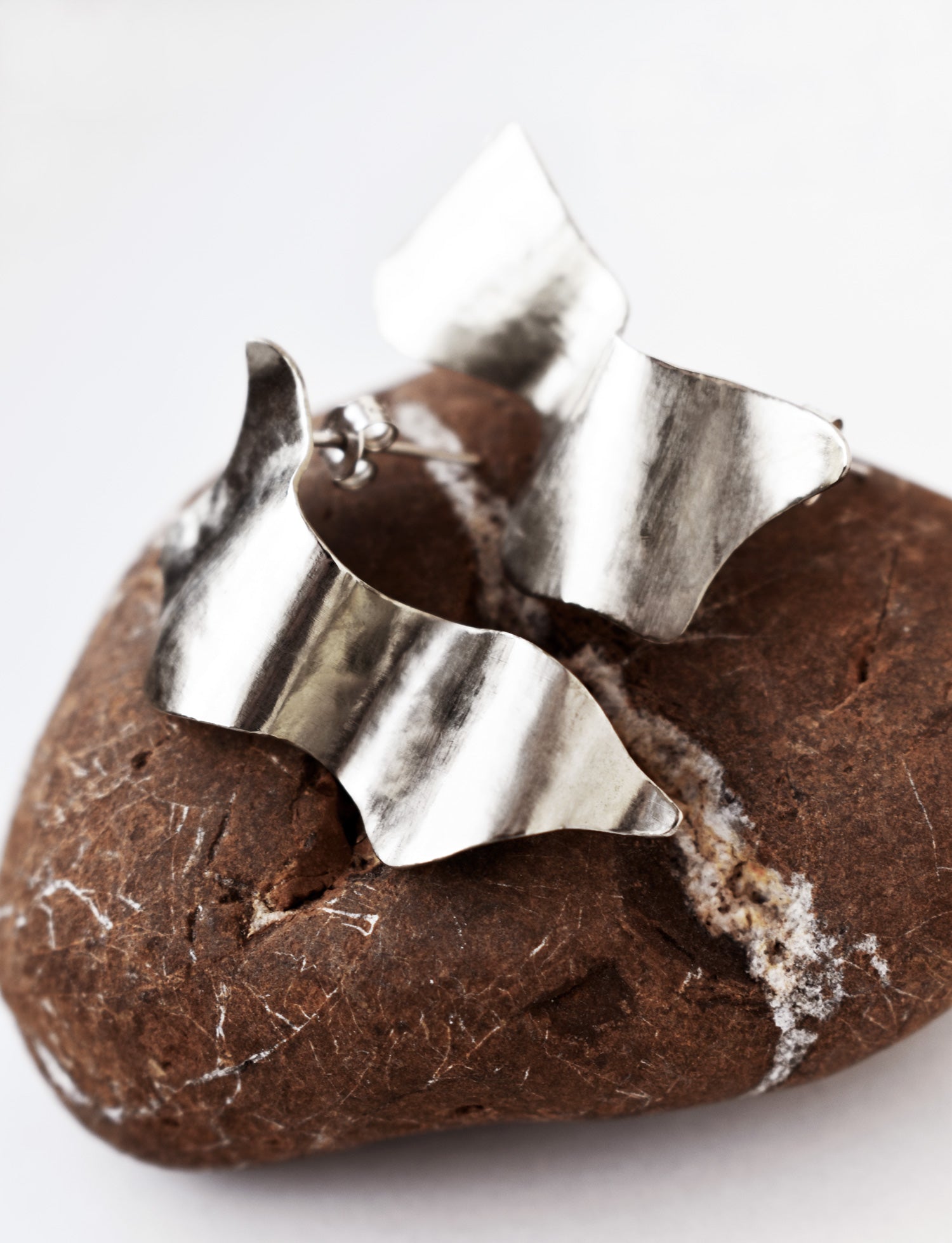 Pair of sculptural silver stud earrings on a textured brown stone