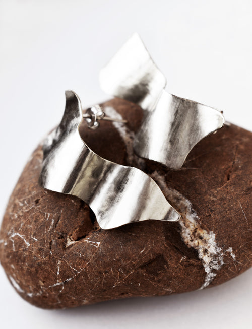Pair of sculptural silver stud earrings on a textured brown stone