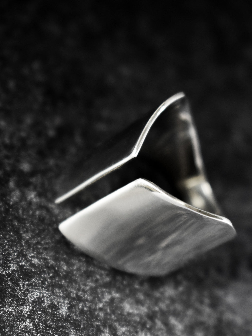Adjustable sculptural silver ring on a dark textured surface