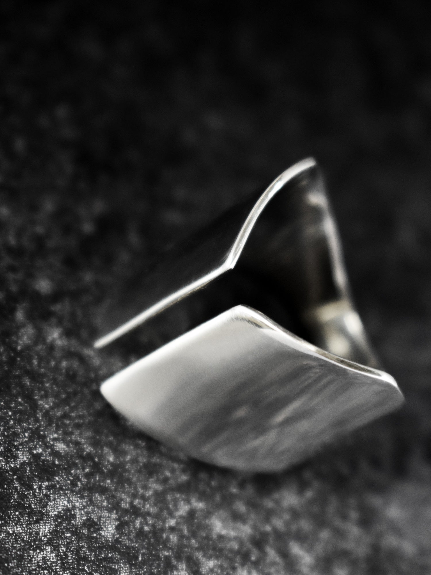 Adjustable sculptural silver ring on a dark textured surface