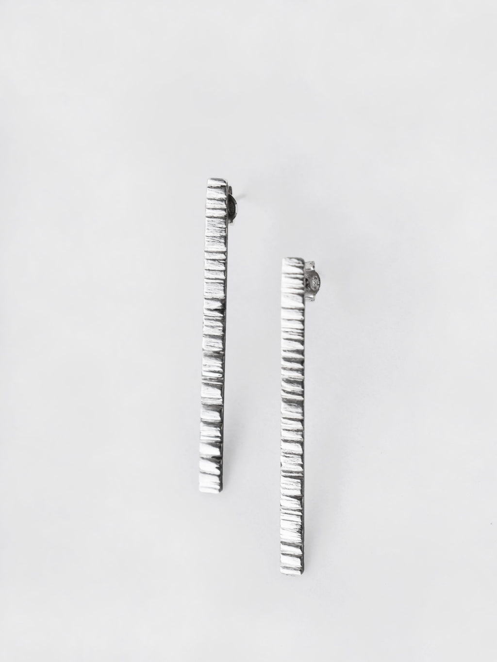 Pair of textured silver bar stud earrings on a light gray background