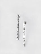 Pair of textured silver bar stud earrings on a light gray background