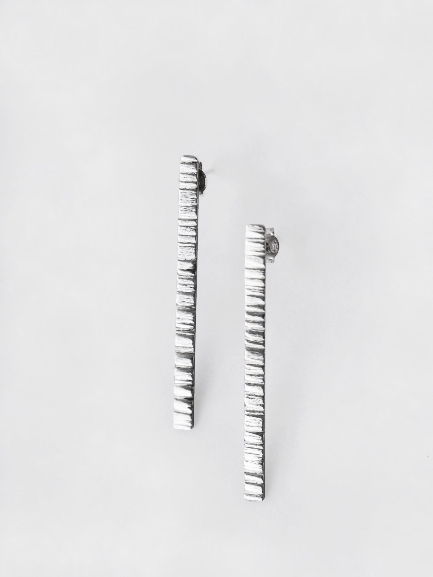Pair of textured silver bar stud earrings on a light gray background