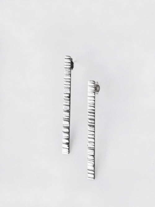 Pair of textured silver bar stud earrings on a light gray background