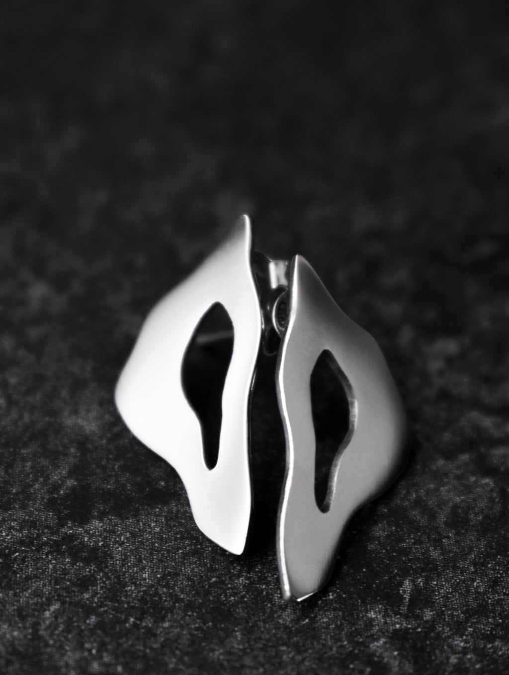 Pair of organic-shaped silver stud earrings with cutout centers on a black textured background