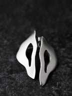 Pair of organic-shaped silver stud earrings with cutout centers on a black textured background