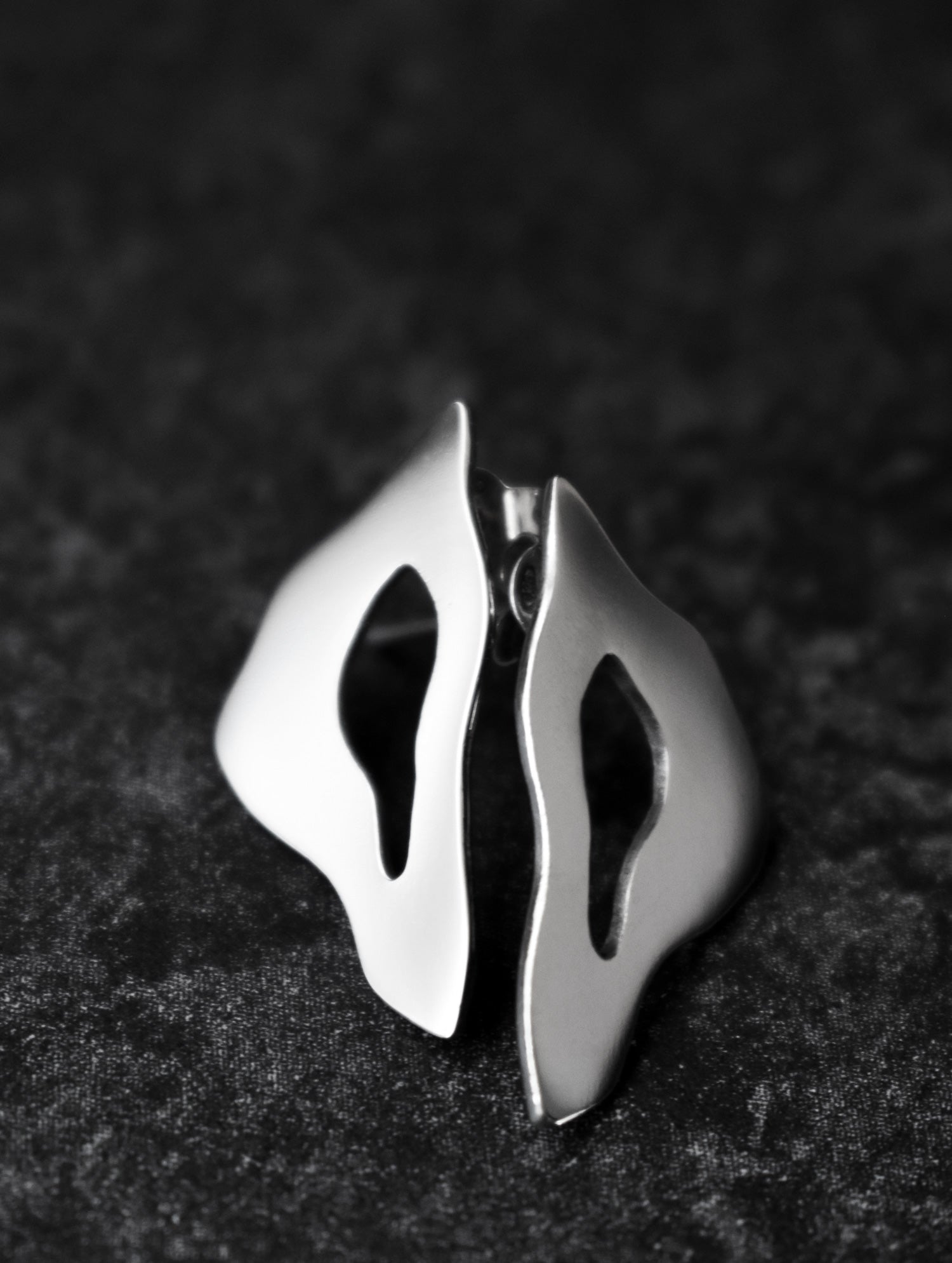 Pair of organic-shaped silver stud earrings with cutout centers on a black textured background