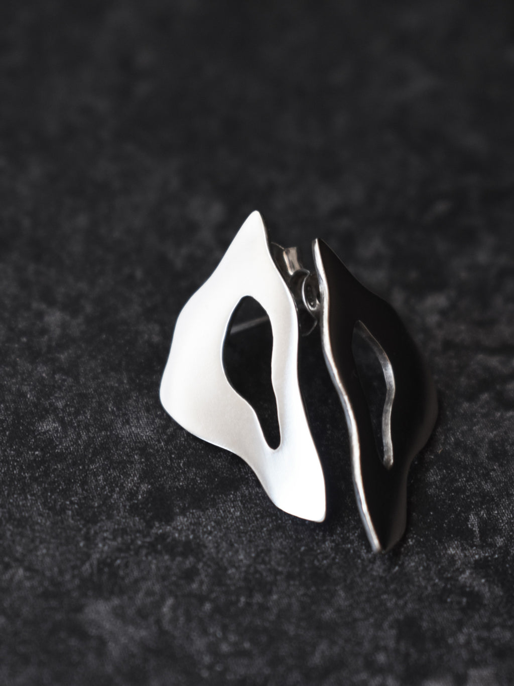 Pair of organic-shaped silver stud earrings with cutout centers on a black textured background