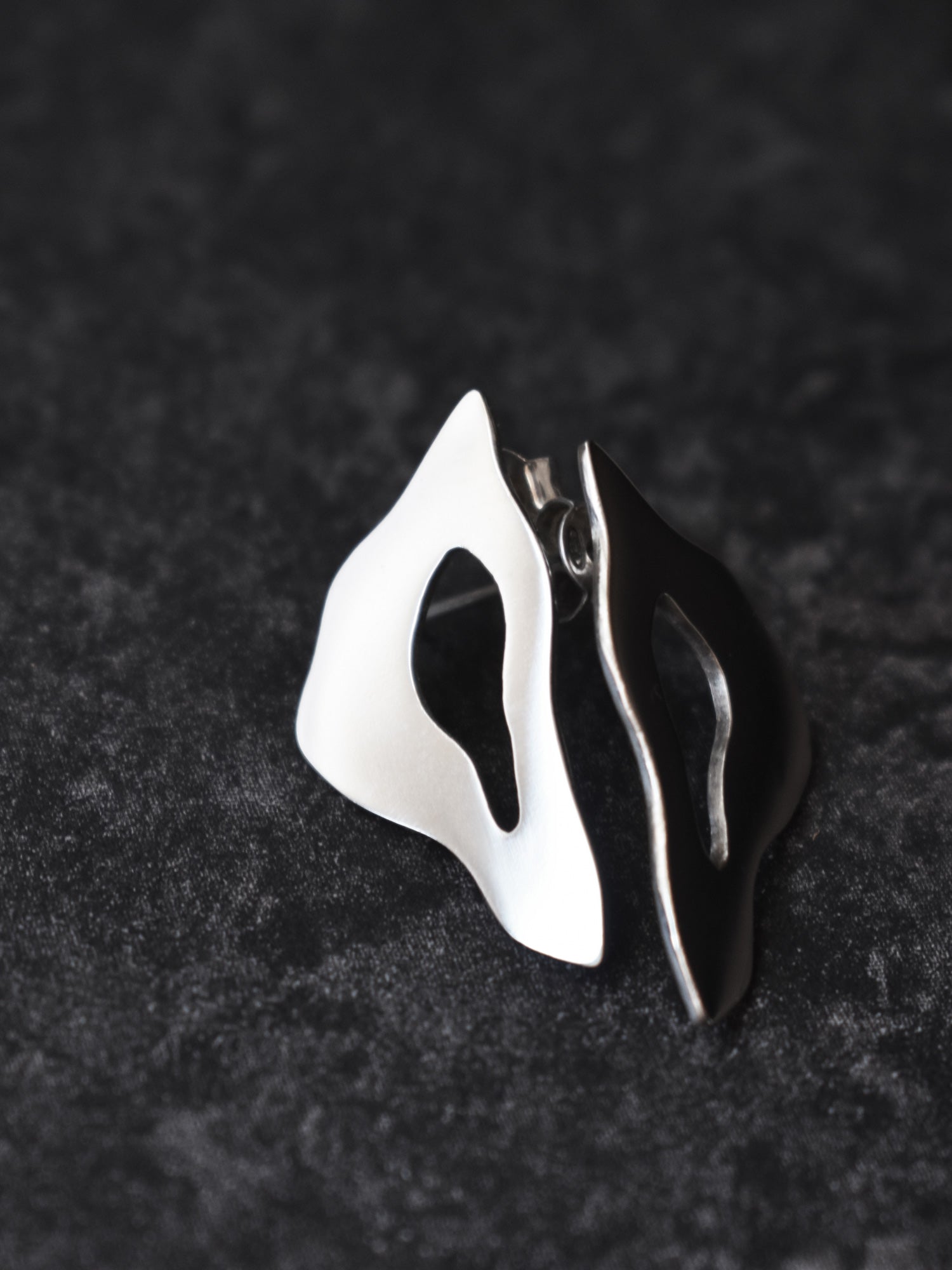 Pair of organic-shaped silver stud earrings with cutout centers on a black textured background