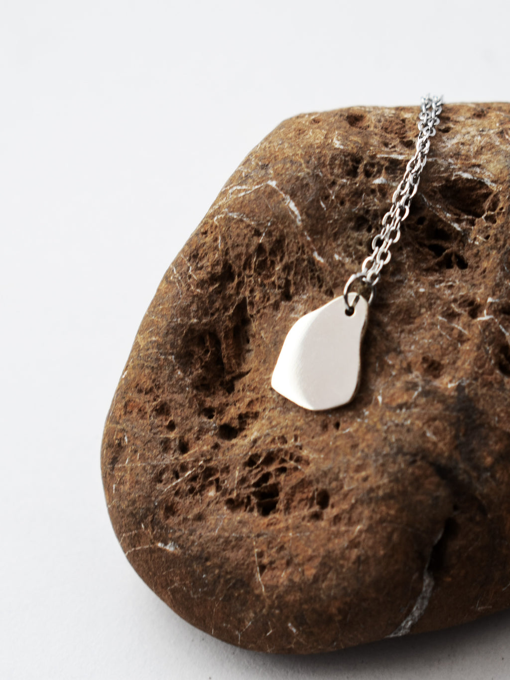 Small silver organic-shaped pendant with chain on a dark textured stone surface