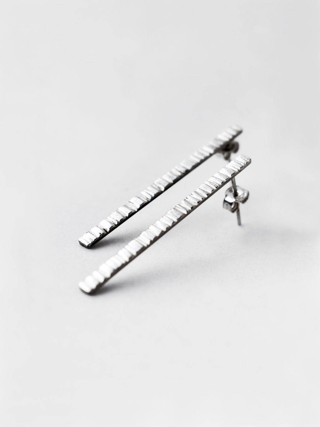 Pair of textured silver bar stud earrings on a light gray background
