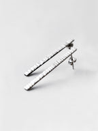 Pair of textured silver bar stud earrings on a light gray background