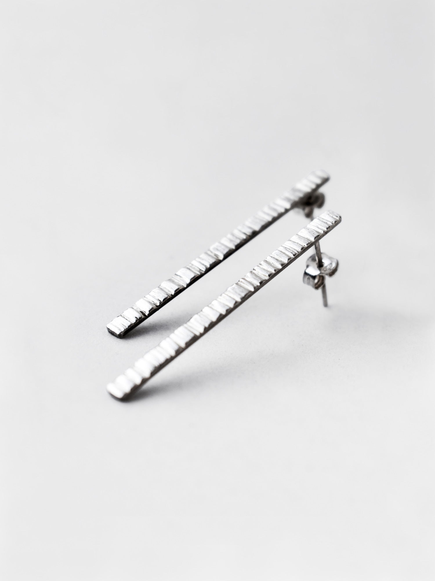 Pair of textured silver bar stud earrings on a light gray background