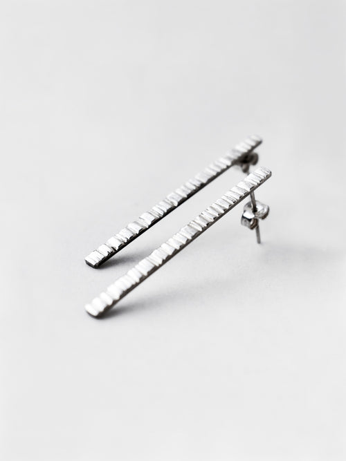 Pair of textured silver bar stud earrings on a light gray background