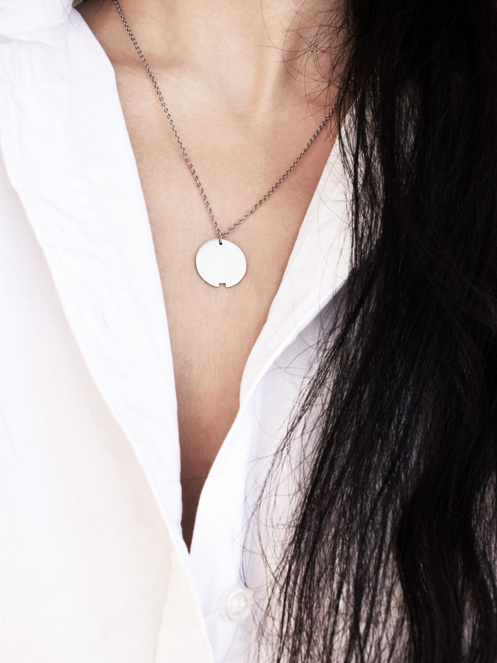 Small silver circle pendant with chain on a woman wearing a white shirt