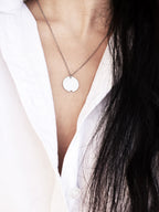 Small silver circle pendant with chain on a woman wearing a white shirt