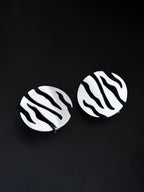 Pair of round silver stud earrings with flowing cutouts on a black background