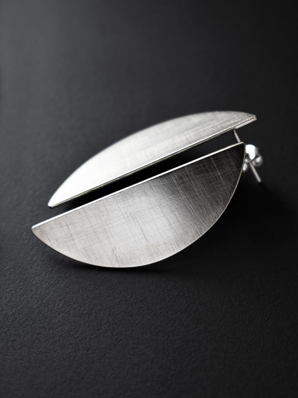 Pair of brushed silver semicircle stud earrings on a black background