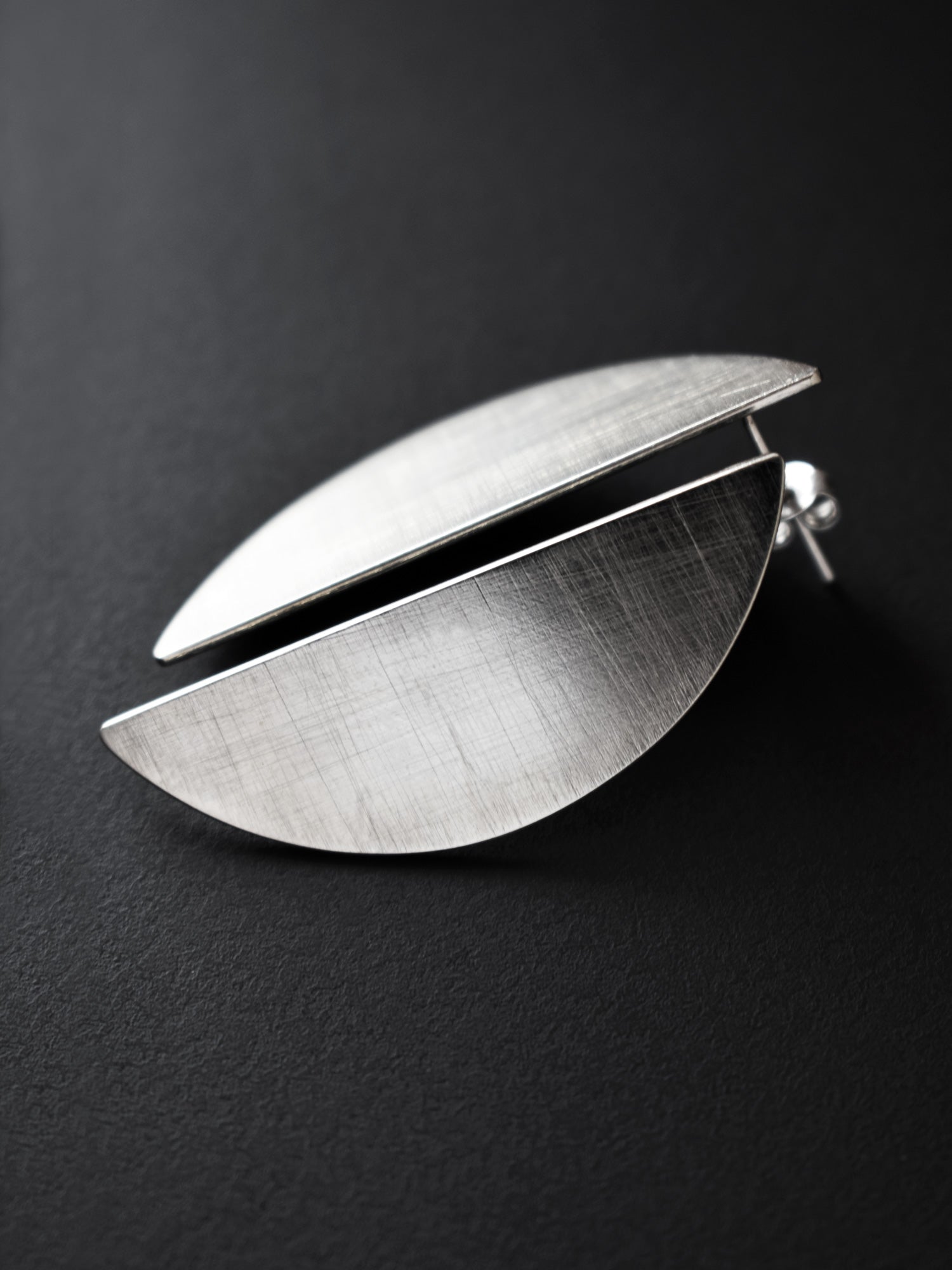 Pair of brushed silver semicircle stud earrings on a black background