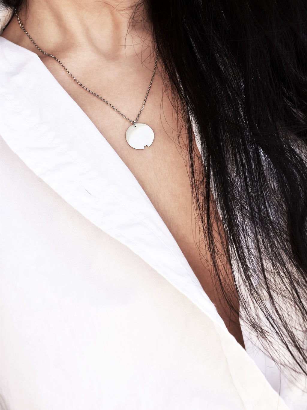 Small silver circle pendant with chain on a woman wearing a white shirt