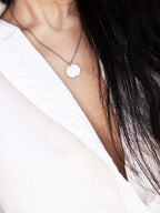 Small silver circle pendant with chain on a woman wearing a white shirt